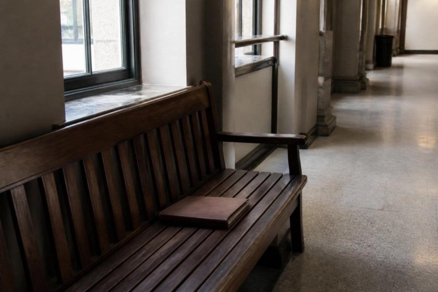A courthouse hallway bench with a closed case folder resting on it, afternoon window light