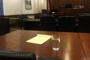A defense counsel table in a Texas courtroom with a legal pad and water glass, soft light