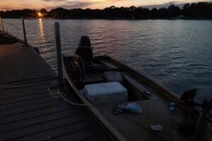 A small fishing boat tied at a lake dock at dusk with a cooler on the deck