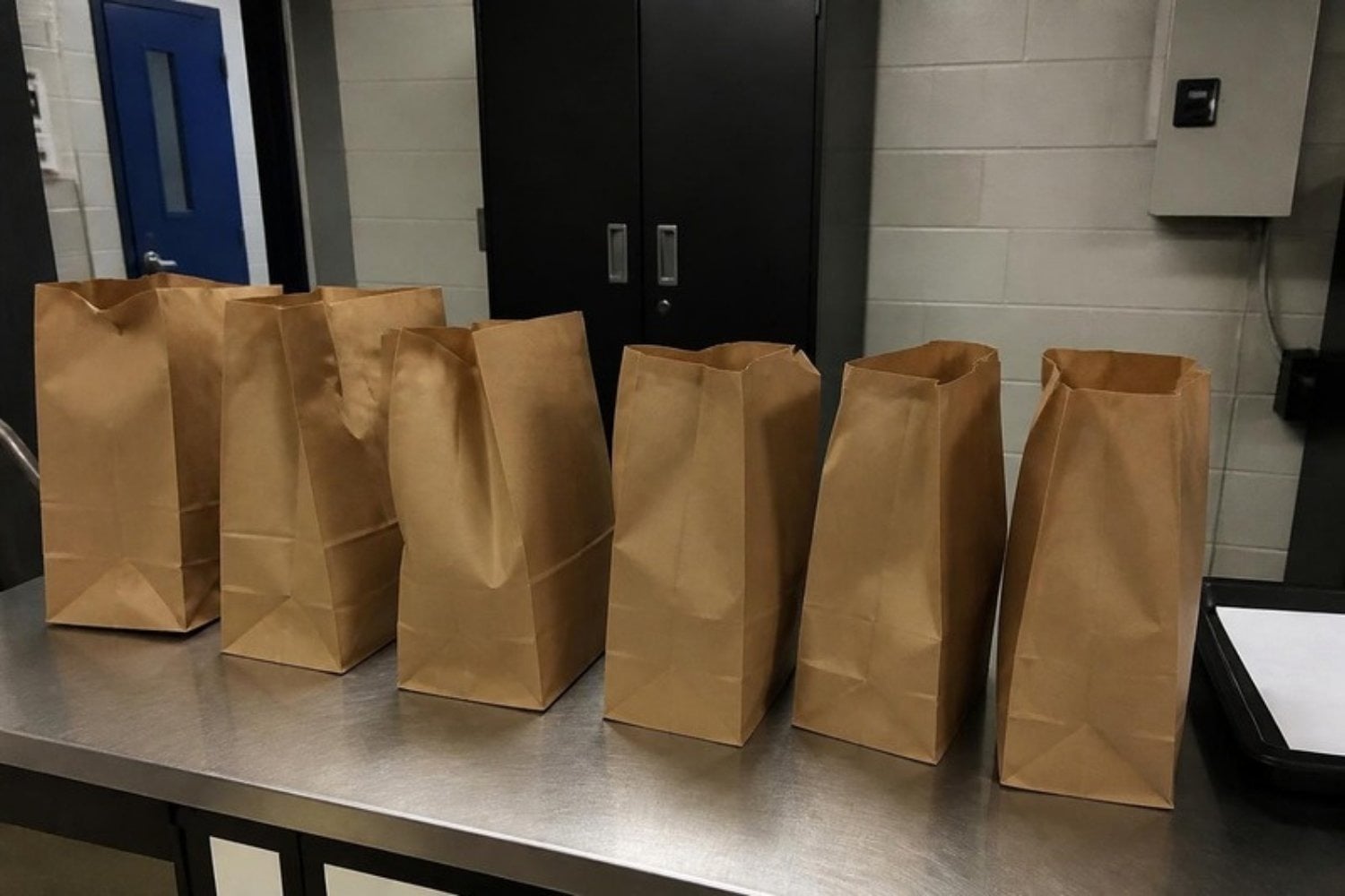 A row of sealed brown paper evidence bags on a police table, overhead light