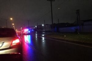A patrol car's flashing lights reflecting on wet pavement behind a stopped car on a Houston street at night