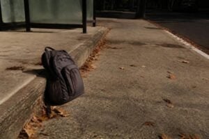 School backpack left on a curb near a bus stop