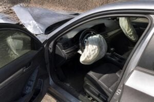 A crashed sedan with airbags deployed seen through the open driver door, daylight