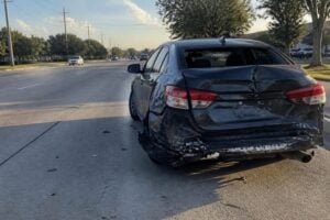A car with a smashed rear end stopped on a wide Pearland suburban road, afternoon light