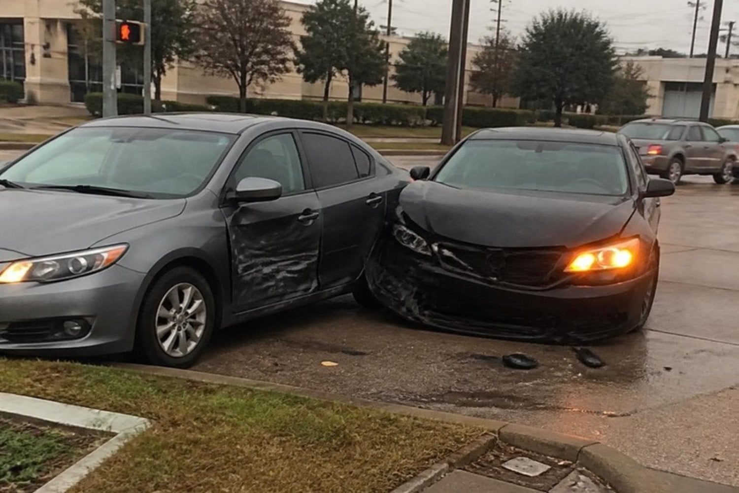 Two cars after a collision at a Houston intersection on an overcast day, hazard lights on