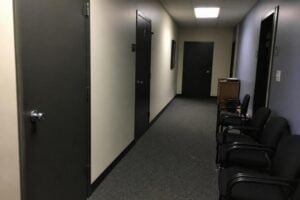 A plain probation office hallway with closed doors and a row of chairs, fluorescent light