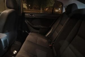 The empty back seat of a car at night with an open beer can on the floor, streetlights through the window